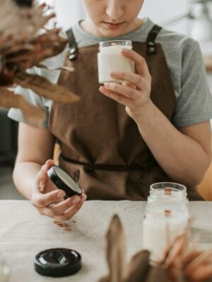 Woman in Gray Crew Neck T-shirt Holding White Candle in Glass Bottle